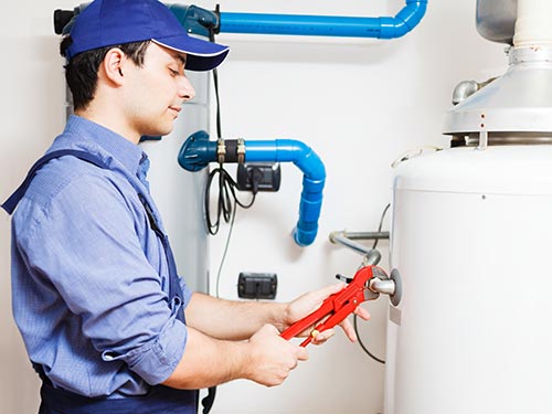 man wearing blue adjusting a white water heater with a wrench