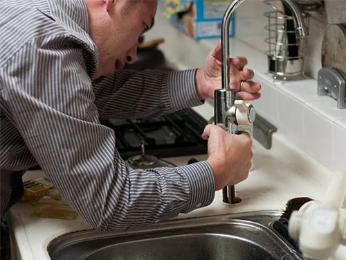 man in striped shirt adjusting the plumbing on a kitchen sink