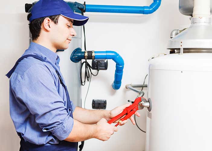 man wearing blue adjusting a white water heater with a wrench